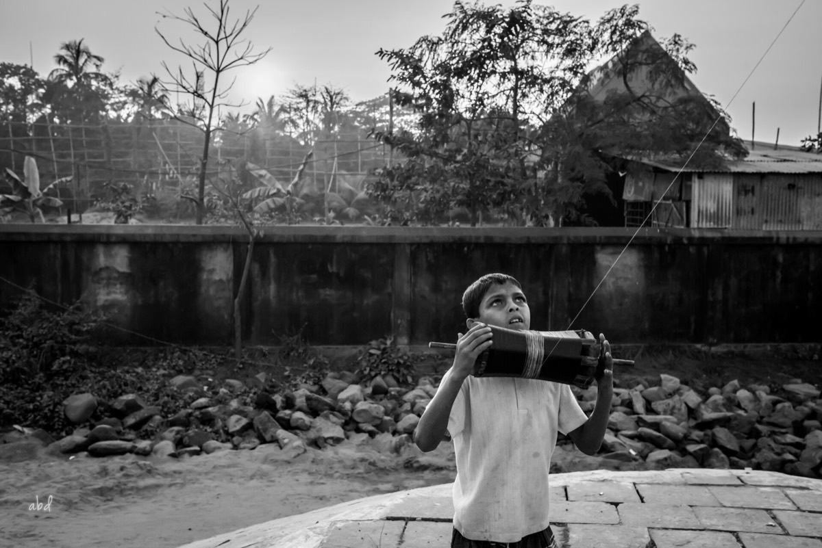 A boy holding a kite reel and watching his kite in the sky in Chittagong, Bangladesh