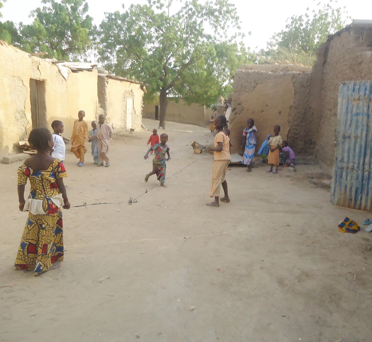 Children playing jump rope together on a sandy village street