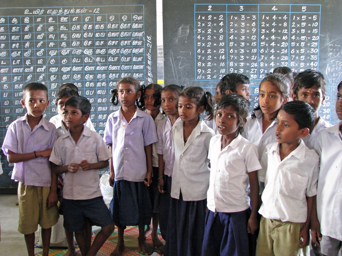 Students in school uniforms standing in front of chalkboards in a classroom in Tamil Nadu, India